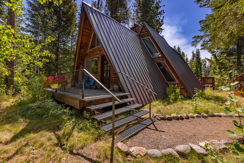A rustic A-frame cabin in McCall, Idaho, with a steep metal roof, wooden siding, and a small front deck surrounded by pine trees and wildflowers on nearly four acres of forested land.