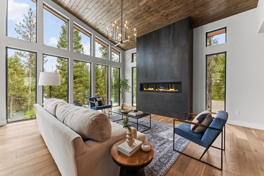 Cozy yet elevated living space featuring a soft neutral sofa, modern blue accent chairs, and panoramic windows framing tall evergreens outside.