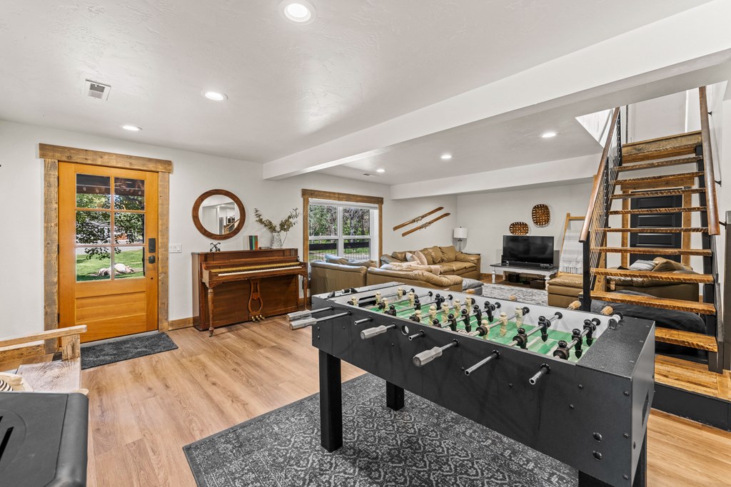 Bright, open living area featuring a foosball table, cozy sectional, wood-accent trim, and stairs with modern railings — perfect for entertaining guests or STR stays.