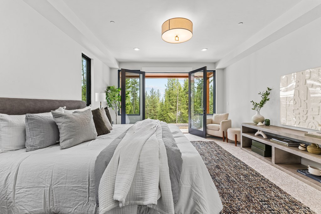Serene primary suite with plush bedding, natural light, and French doors opening to a covered patio with tree-lined views.