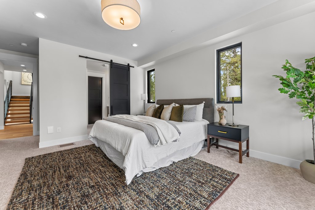 Spacious main bedroom featuring a textured area rug, barn door, and soft modern decor that highlights the home’s warm minimalist aesthetic.
