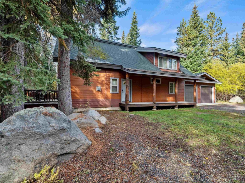 Front exterior of 1034 Fireweed Drive in McCall, Idaho — a classic mountain cabin surrounded by pine trees with a Trex deck and natural wood finishes.
