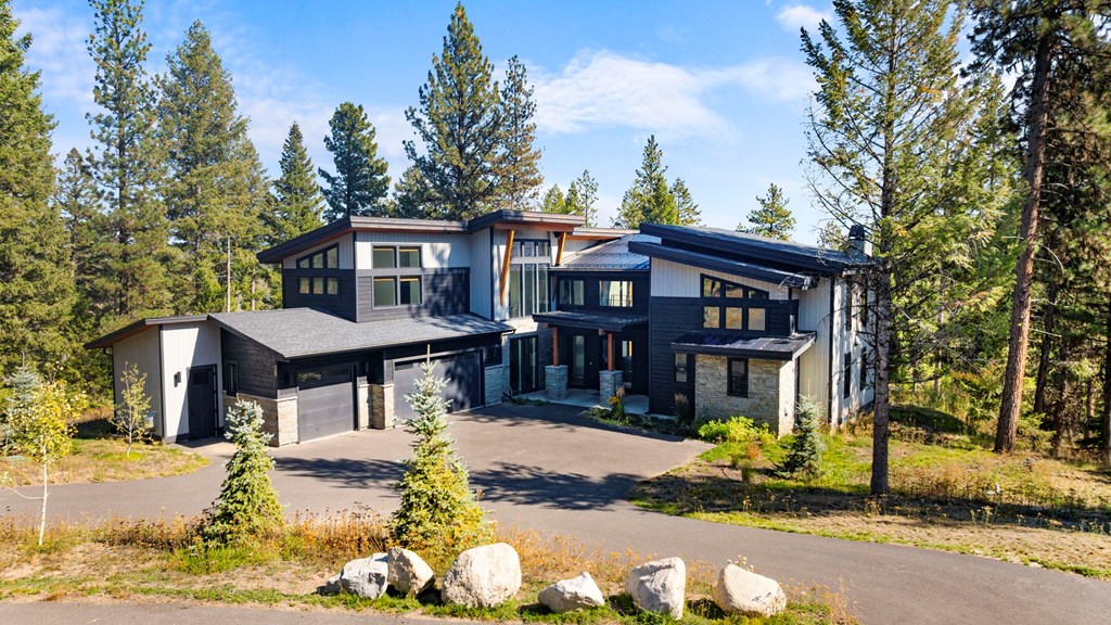 Contemporary mountain modern home at 38 Bella View Lane in McCall, Idaho. Showcases the bold architecture, metal rooflines, and natural stone accents surrounded by pines.