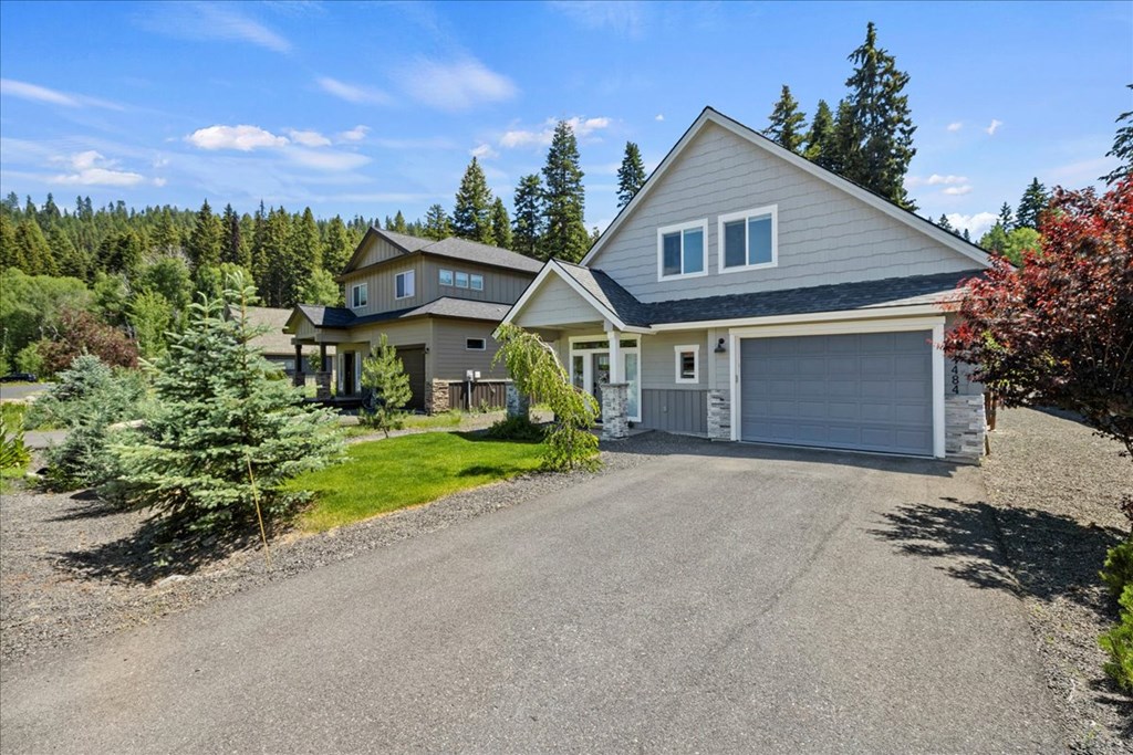 Front exterior of a modern mountain home at 1484 Dragonfly Loop in McCall, Idaho. This McCall real estate listing features gray siding, a two-car garage, landscaped yard, and views of surrounding pine trees under a clear Idaho sky.