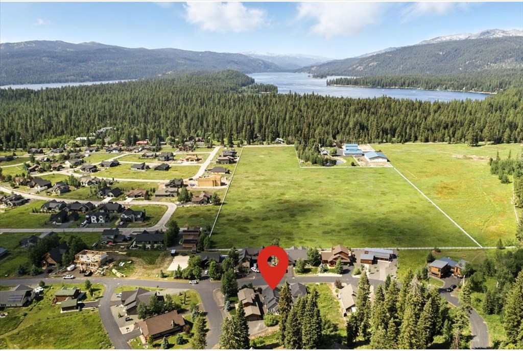 Aerial photo of 1484 Dragonfly Loop in McCall, Idaho, marked with a red location pin. The McCall real estate property is shown surrounded by pine trees, open meadows, and nearby neighborhoods with Payette Lake and surrounding mountains visible in the distance—highlighting the home’s proximity to McCall’s outdoor recreation and lakefront lifestyle.