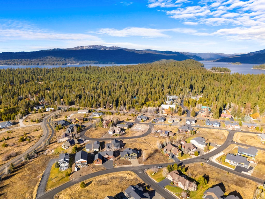 Drone view of the Lick Creek Meadows neighborhood in McCall, Idaho with Payette Lake, dense pine forest, and surrounding mountains in the distance.