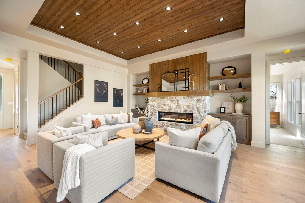 Bright living room in a McCall Idaho new construction home featuring a linear stone fireplace, wood-paneled ceiling with recessed lights, and modern neutral furniture.