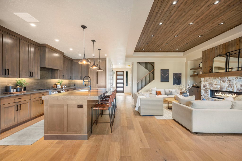 Open-concept kitchen and great room with long wood island, warm wood cabinets, pendant lighting, and adjoining living area with fireplace in a McCall, Idaho home.