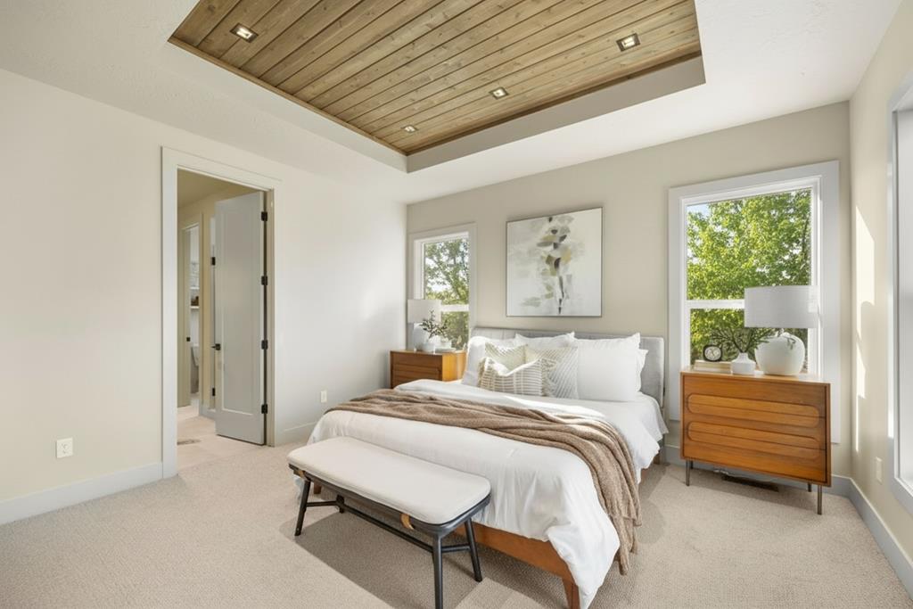 Primary bedroom with tray wood ceiling, large windows, neutral bedding, and mid-century style nightstands in a McCall, Idaho new construction house.