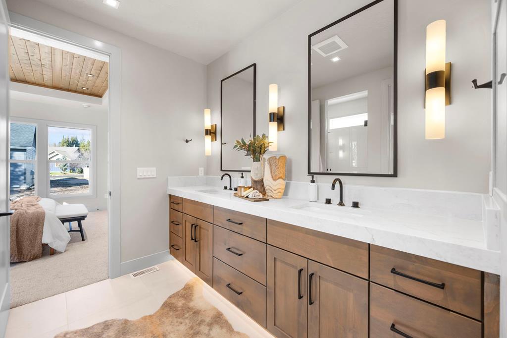 Primary bathroom with double-sink vanity, quartz counters, wood cabinetry, modern sconces, and a view back into the bedroom of the McCall Idaho home.