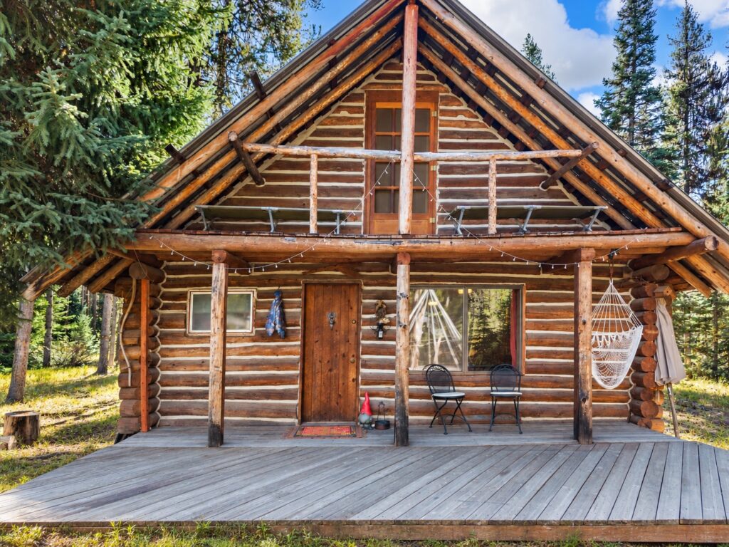Front of the 1980 log cabin with a full-width covered porch, hammock chair and gable balcony