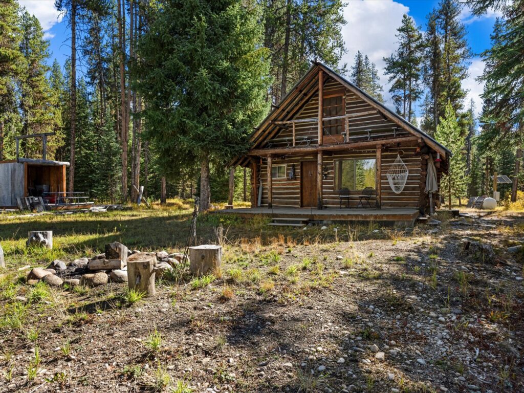 The log cabin seen across the yard, with stump seating around the stone fire ring