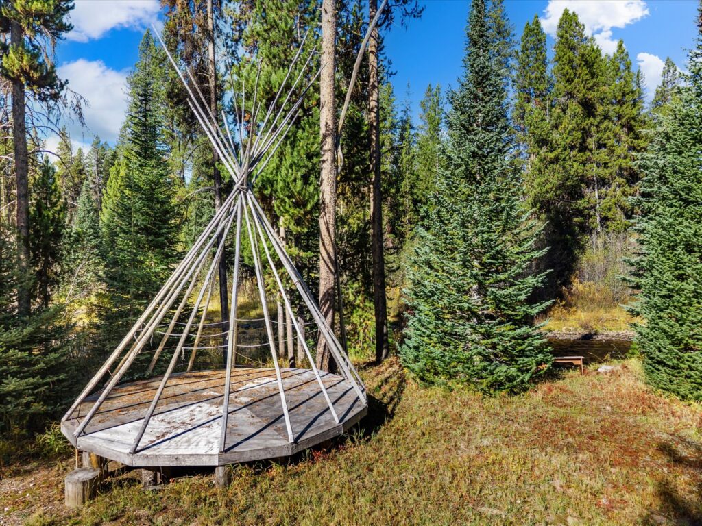 Teepee frame on a raised wooden platform among the pines, ready for canvas or summer camping