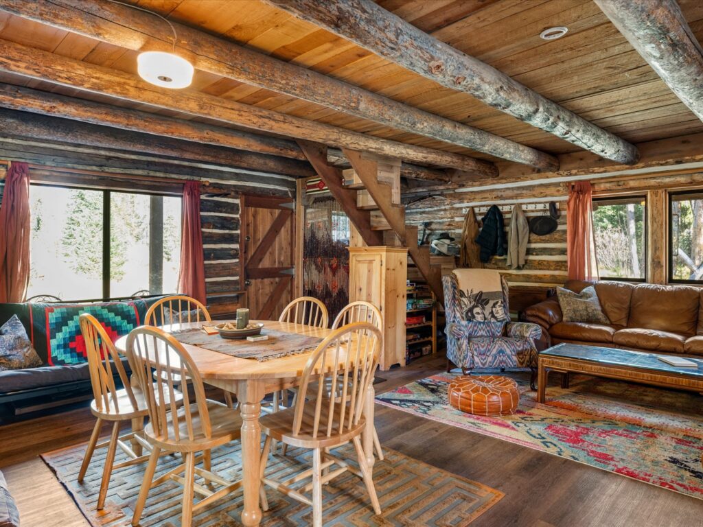 Open main floor of the log cabin with a dining table, leather couch, log walls and beamed ceiling