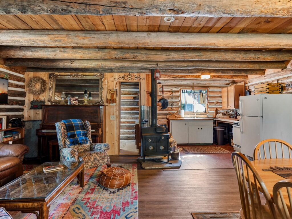Main floor looking toward the wood stove, upright piano and kitchen in the open log cabin