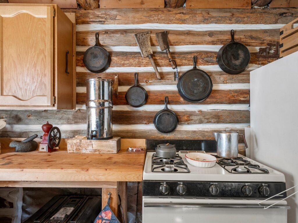 Gas range beneath a wall of hanging cast iron cookware in the log cabin kitchen