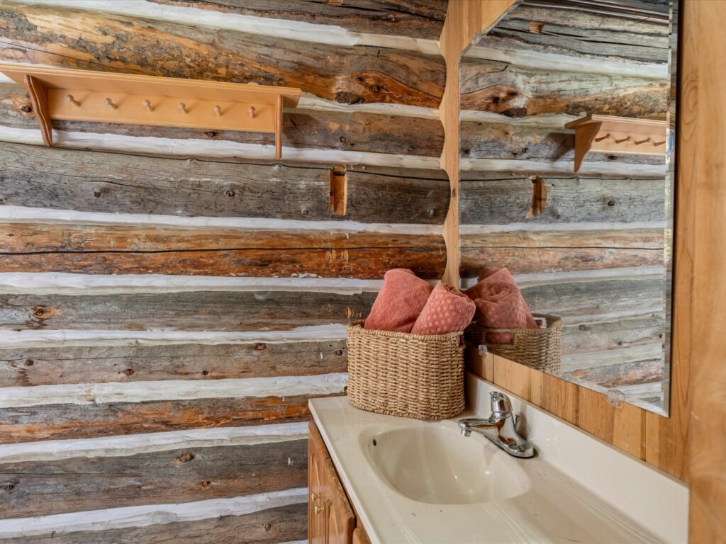 Bathroom vanity sink with a basket of towels against a log wall
