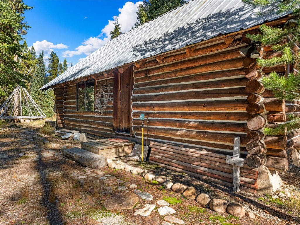 Hand-hewn log wall with a stone-edged walkway and the teepee in the background