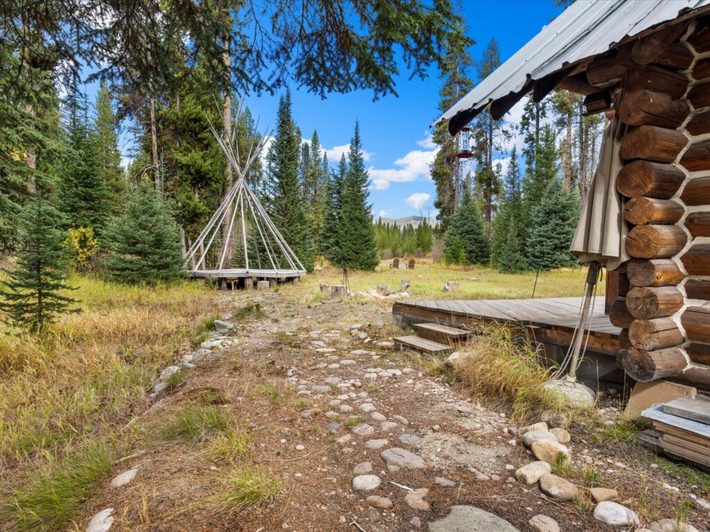 Stone path past the cabin porch toward the teepee and meadow